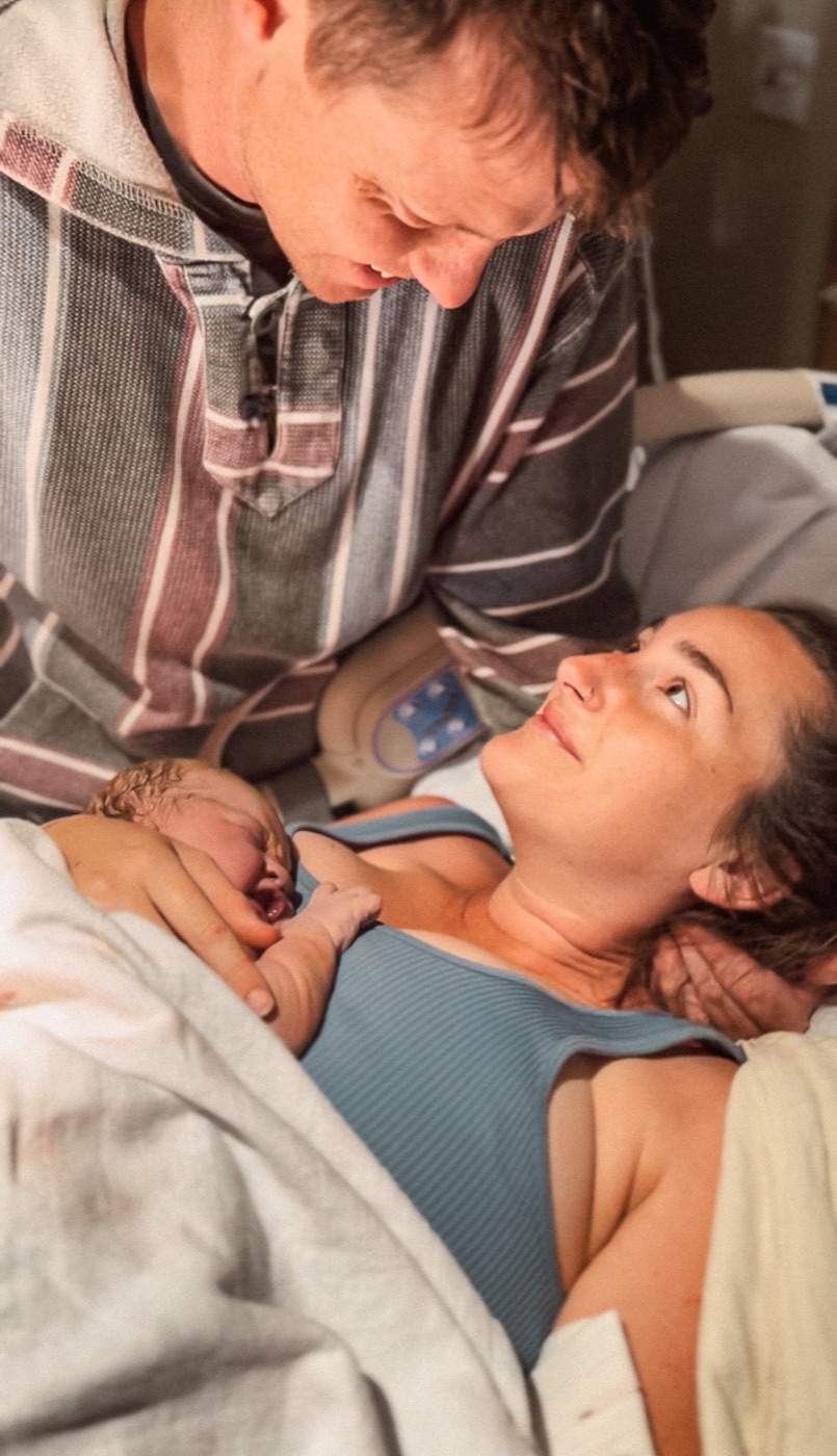 Father leaning over mother holding their newborn baby in the hospital
