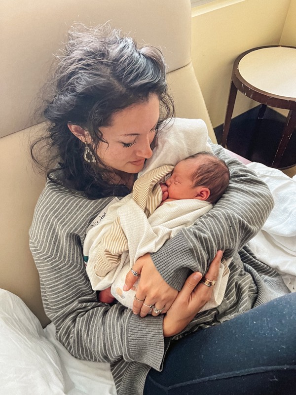 Juliana in a striped sweater holding a newborn in a hospital setting